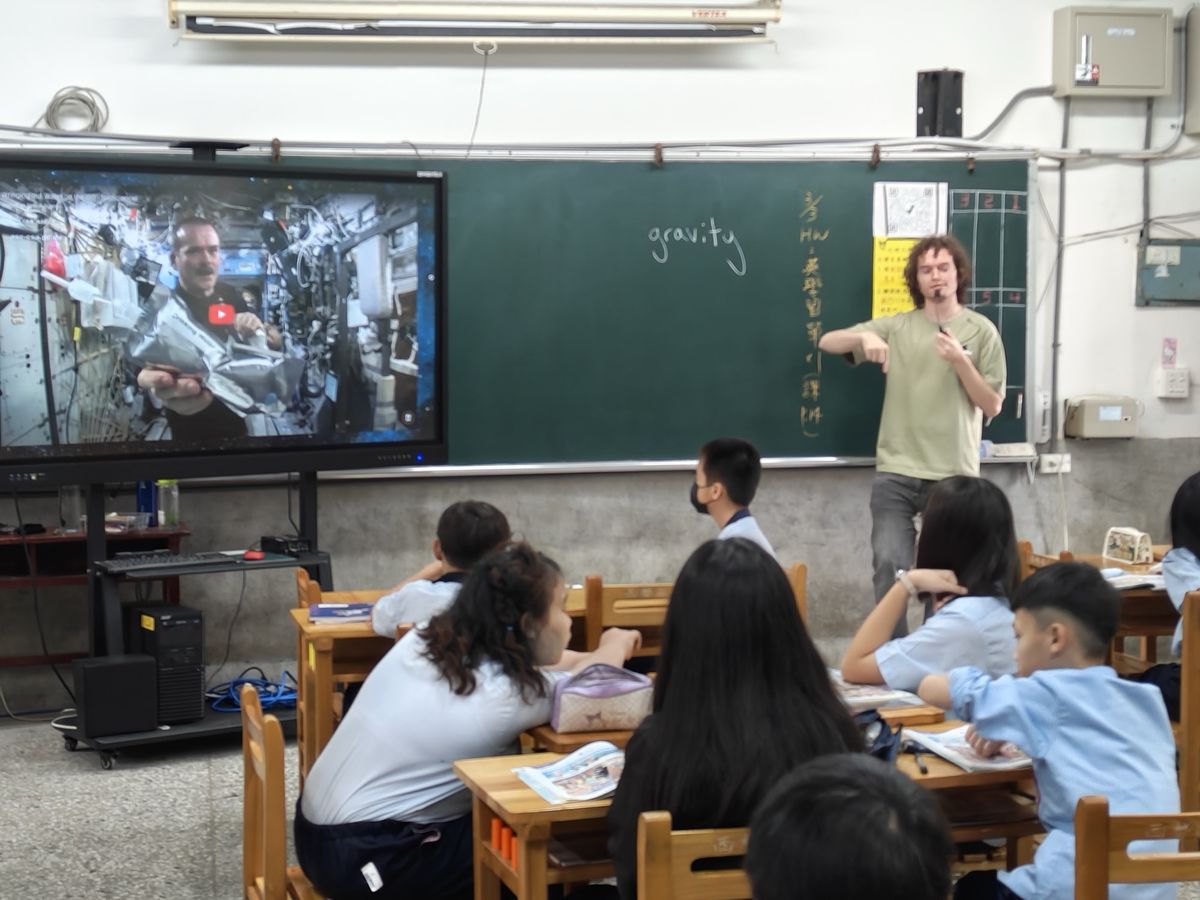 外師 Taylor 在五年級教室介紹太空生活，螢幕上是太空站裡的太空人