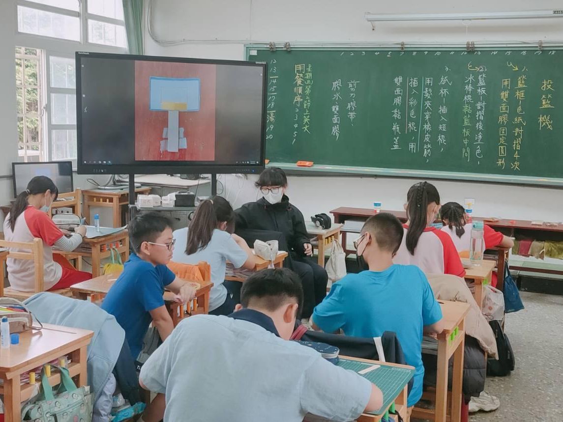 學生在教室裡動手製作紙杯投籃機，螢幕上是投籃機的圖片