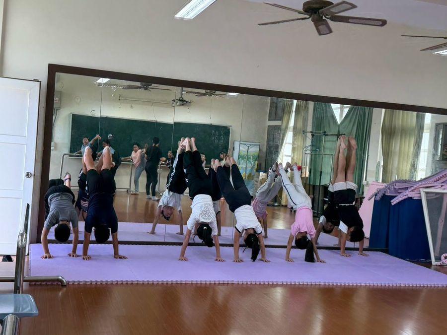 舞蹈隊學生在鏡子前的墊子上練習倒立 Dance-team students practising handstands on a mat in front of the studio mirror