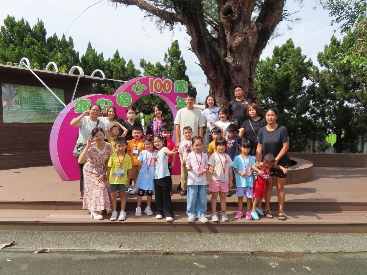 源泉國小新生與家長、老師在「源泉國小100週年」粉紅色圓形看板前大合照 Yuanchyuan's new first-graders with parents and teachers in a group photo by the school's 100th-anniversary sign