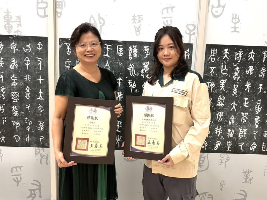林淑貞校長與同仁在書法牆前，手捧兩幅裱框的感謝狀 Principal Lin and a colleague holding two framed certificates of thanks by the calligraphy wall