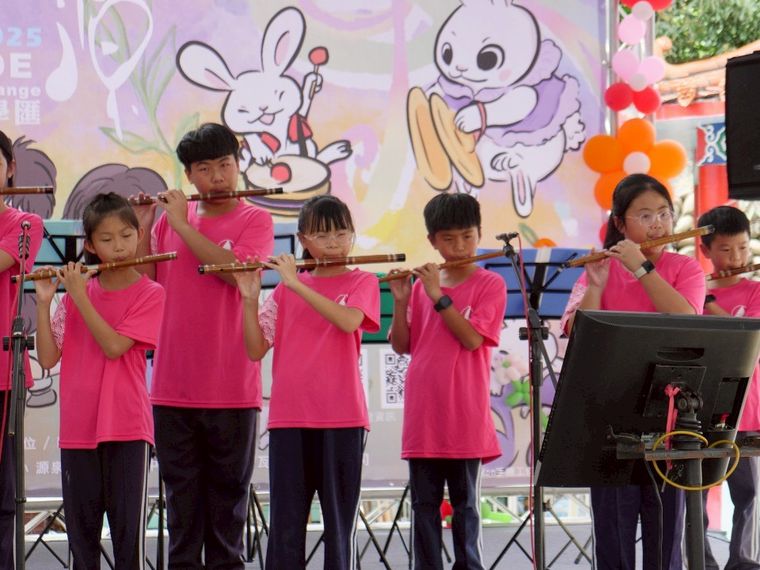 源泉國小中國笛社學生穿著粉色社服，在舞台上看譜吹奏笛子 Yuanchyuan Chinese-flute club students playing the flute on stage