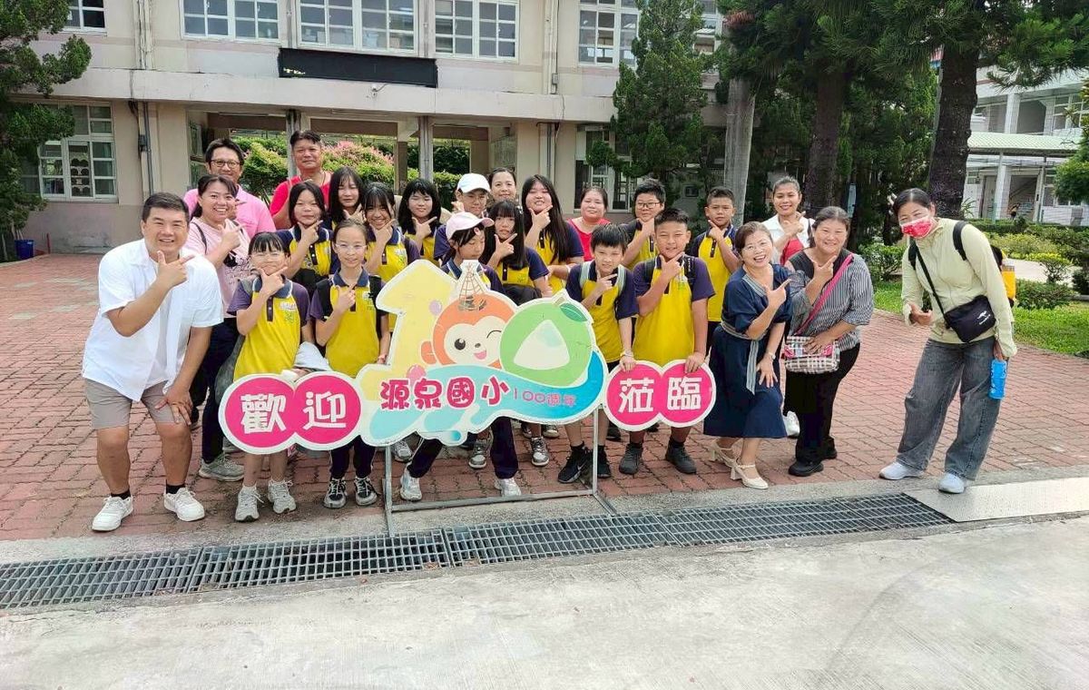 源泉國小師生在校門前的「歡迎源泉國小 100 週年蒞臨」看板旁大合照 Yuanchyuan students and teachers in a group photo by the school's 100th-anniversary welcome sign at the front gate