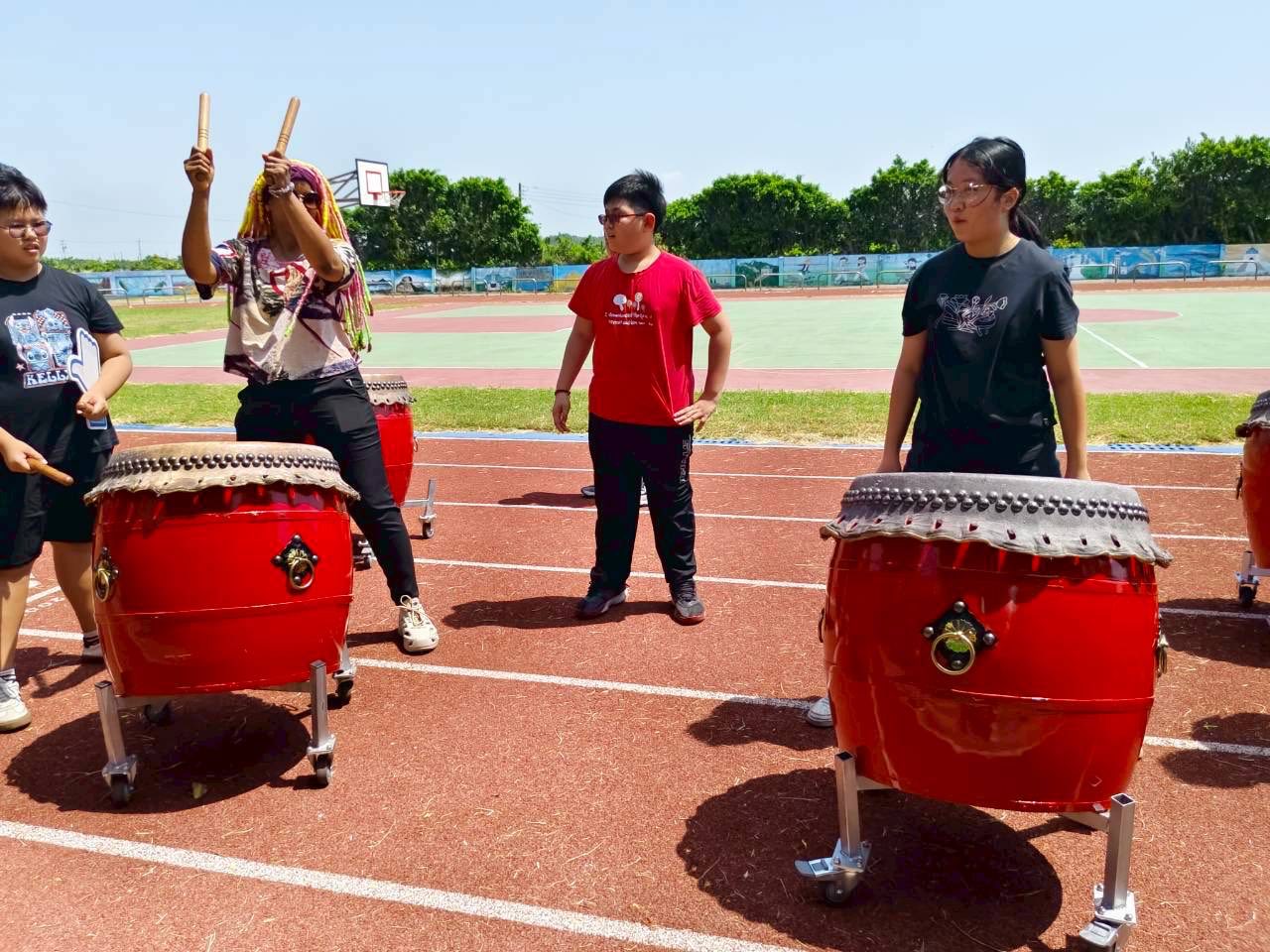 Yuhua students drumming up close, sticks raised high over the red taiko drums