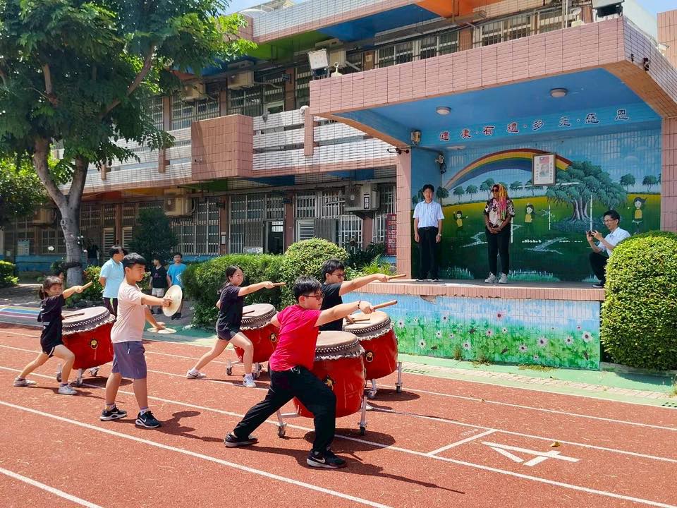 Yuhua students performing on red taiko drums on the running track as the principal and Dom Jones watch from the stage