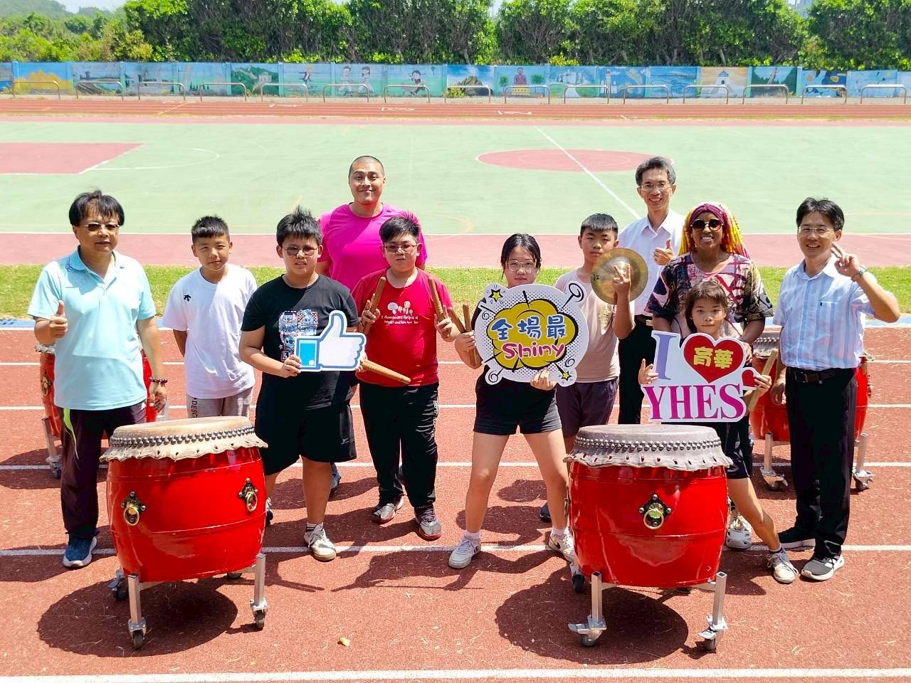 Group photo of students and teachers with the drums, holding I love YHES and Shiny placards