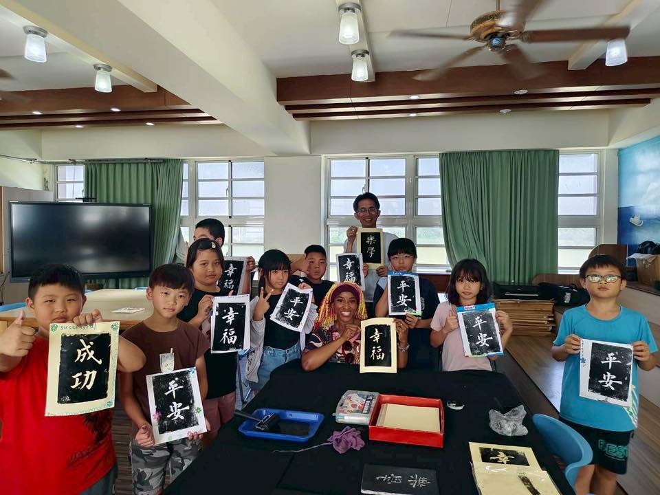 Children holding their finished ink-rubbing prints reading Success, Peace and Happiness in Chinese