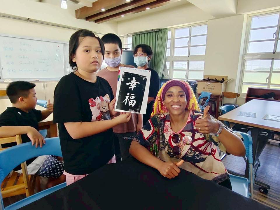 A student holds up a Happiness ink-rubbing print while Dom Jones gives a thumbs up
